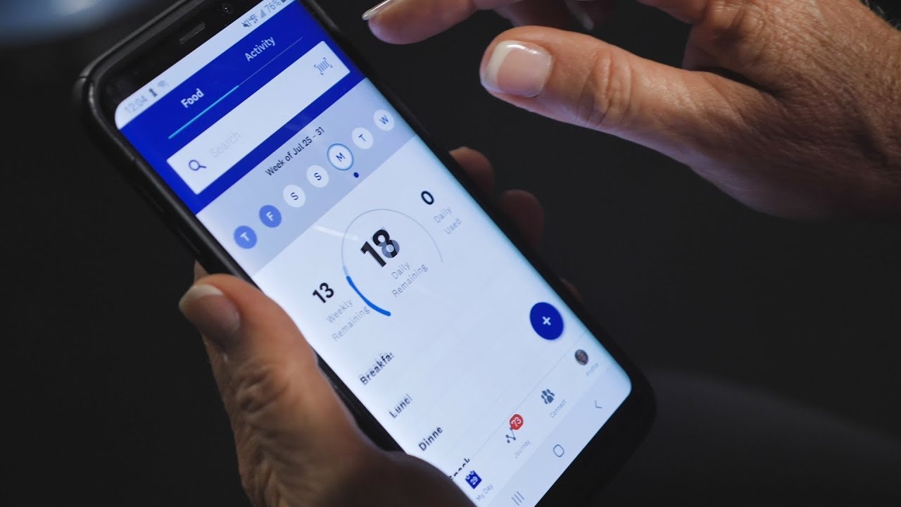 Handen die een dieetschriftje en telefoonapp vasthouden